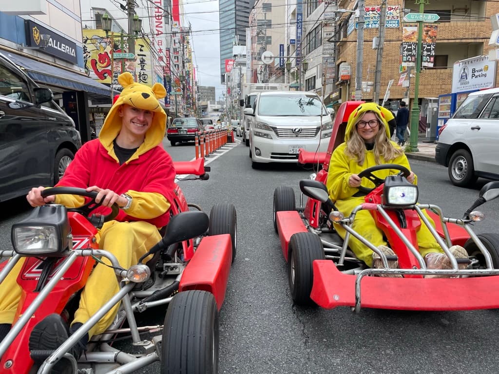 Two people in fancy dress sat in go-karts on an Osaka street